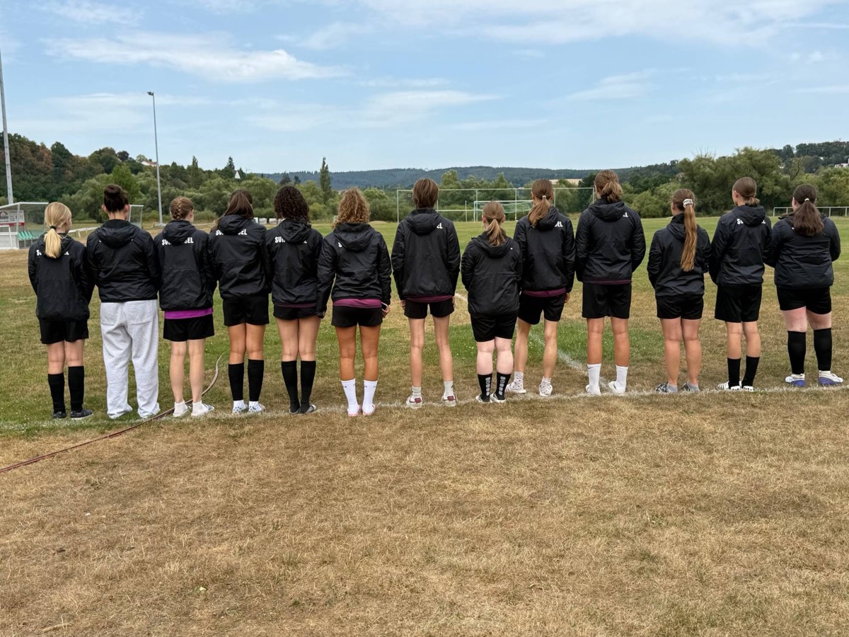 Die B-Juniorinnen der SVH Kassel stehen von hinten fotografiert in einer Reihe am Spielfeldrand, alle in den neuen schwarzen Regenjacken mit Vereinsaufdruck